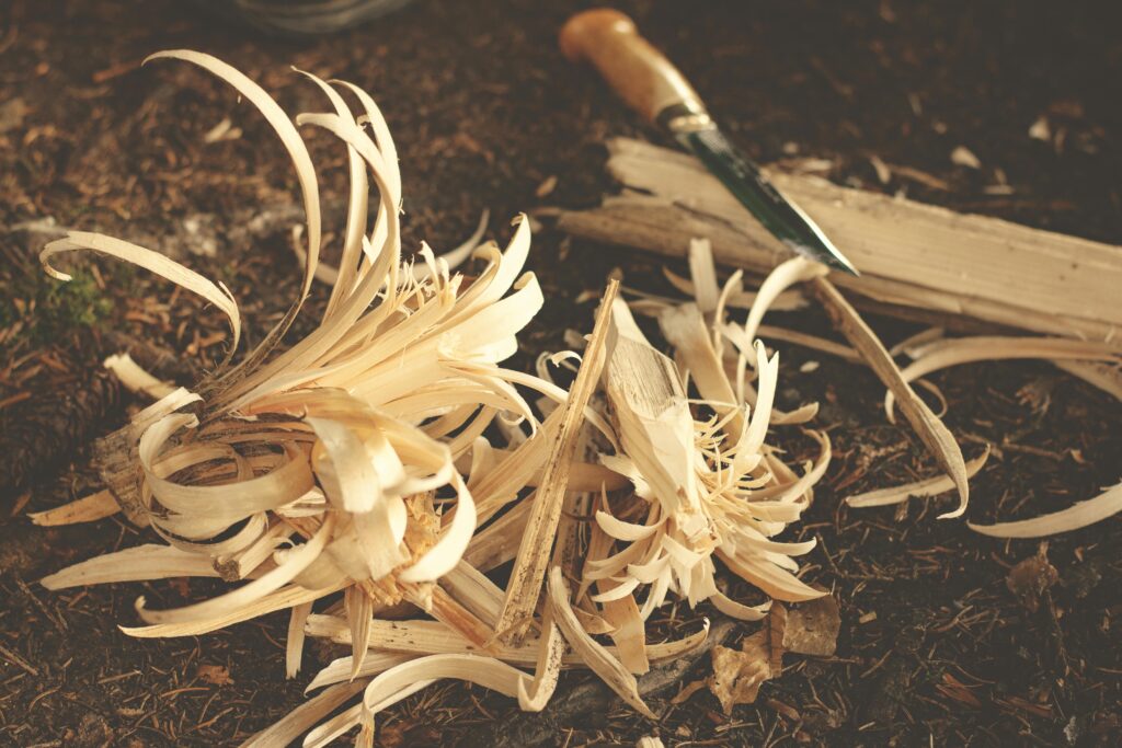 Woodworking knife and wood shavings on ground, showcasing craftsmanship in a rustic outdoor environment.